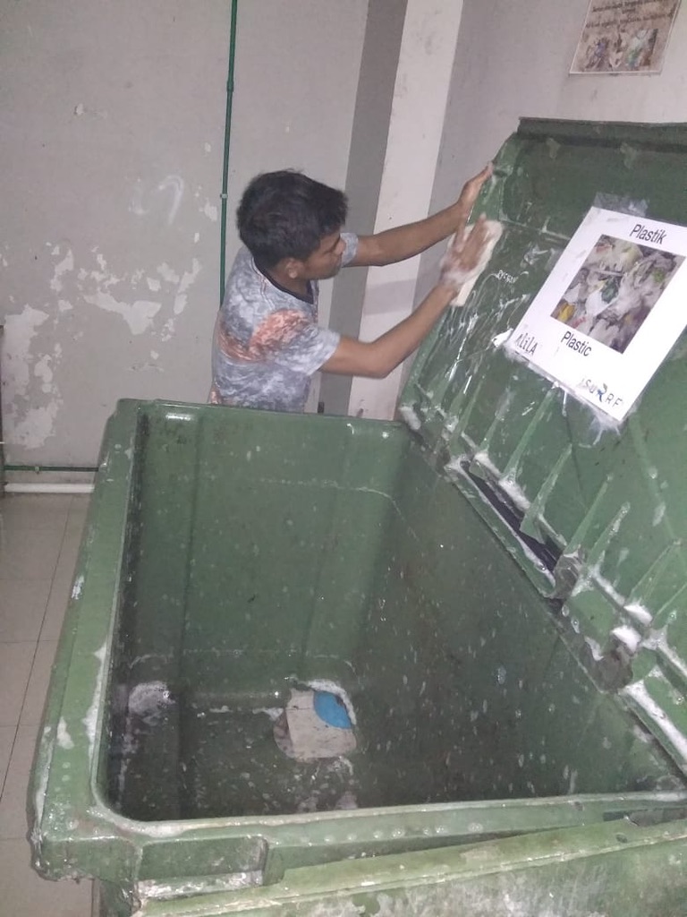 Image 38. Person washing a large green plastic bin with soap
