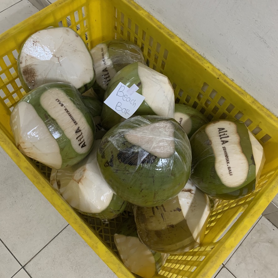 Image 18. Yellow crate of young coconuts branded Alila Seminyak, each wrapped in clear plastic film, with a Beach Bar note