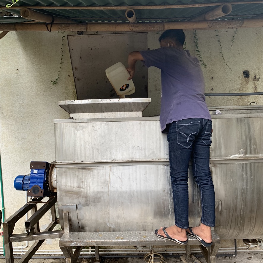 Image 23. Person pouring from a jerrycan into a large stainless steel organics machine