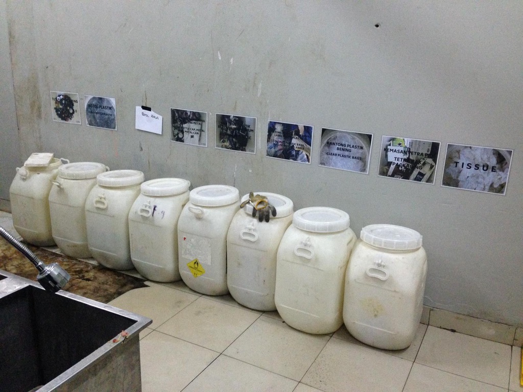 Image 10. White drums under wall labels with photographs of material streams