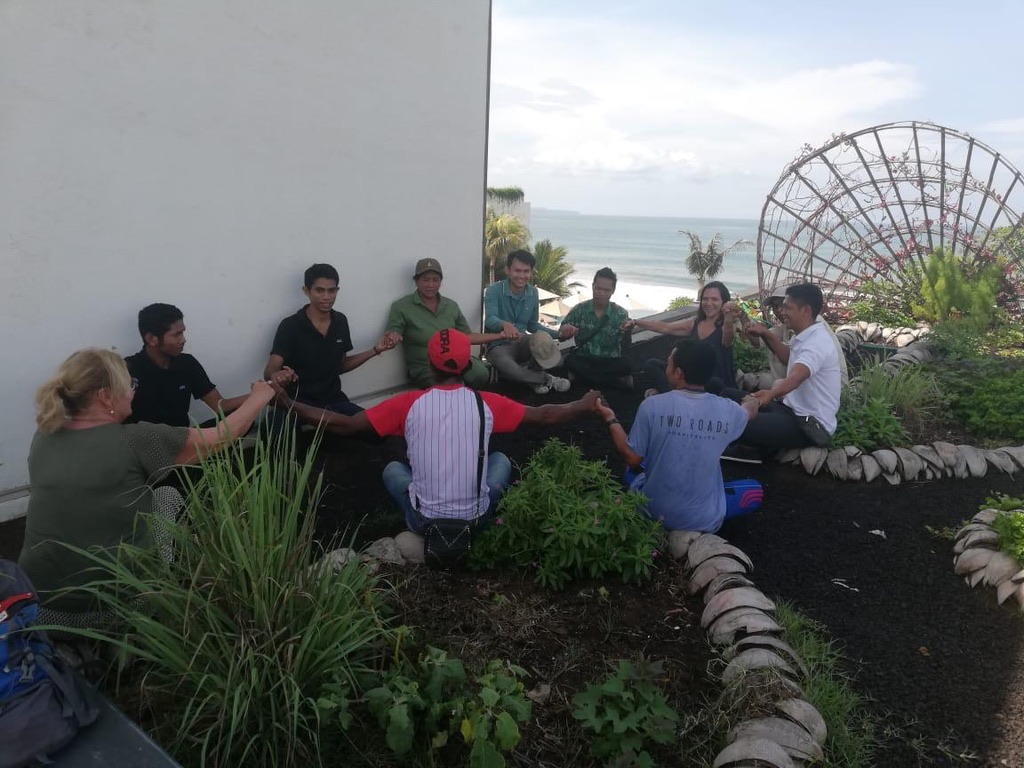 Image 2. Team sitting in a circle holding hands in a rooftop garden overlooking the ocean