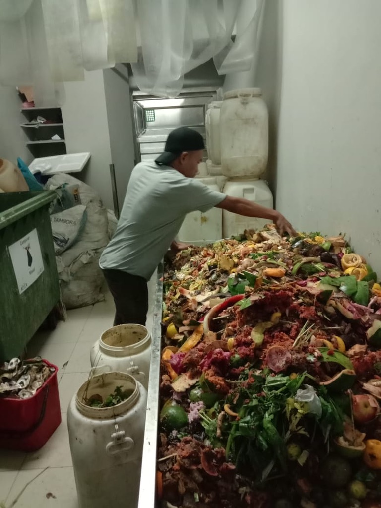 Person sorting a long trough of mixed wet food organics